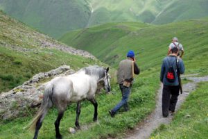 Menschen wandern mit Pferd durch grüne Berglandschaft im Kaukasus